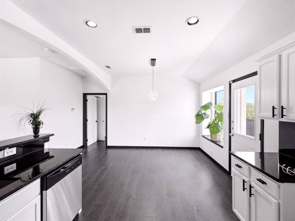 Kitchen featuring dark stone countertops, white cabinetry with matte black hardware, stainless steel dishwasher, wood-finish flooring, and a recessed window ledge
