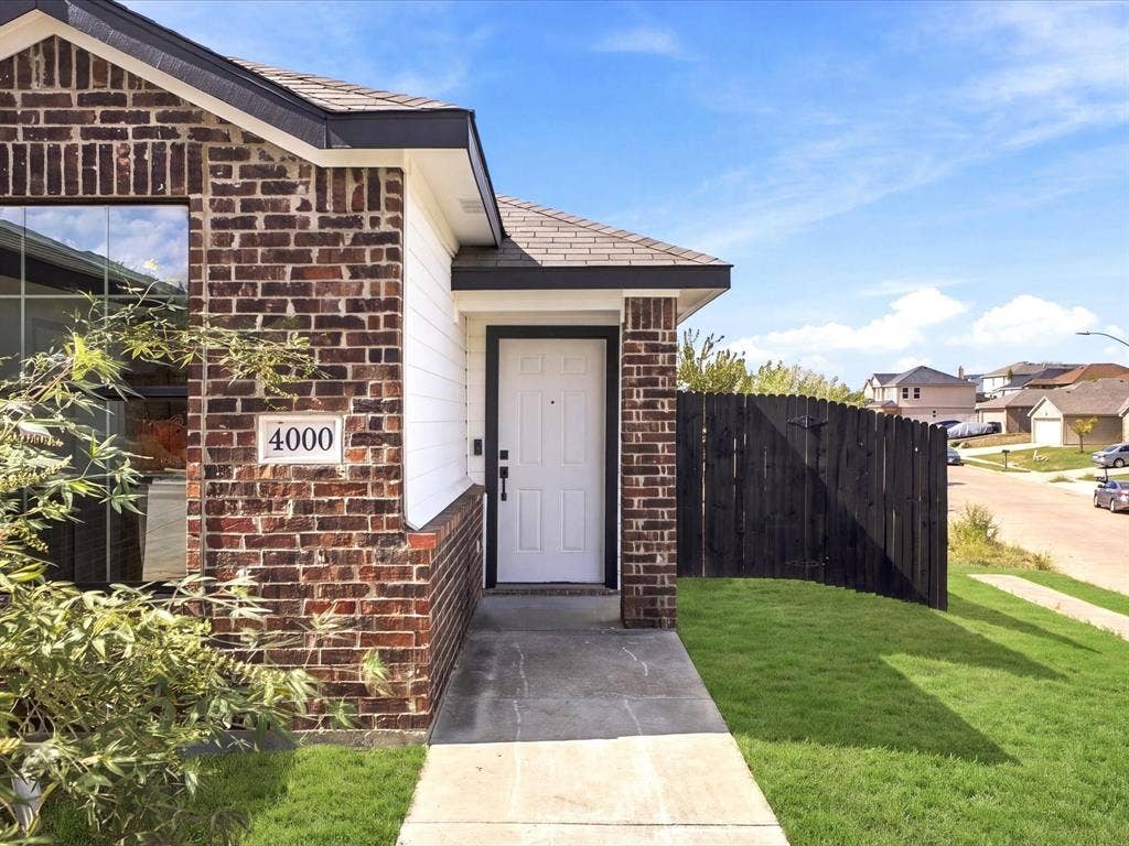 Exterior facade featuring multi-tonal brickwork, horizontal siding, a concrete walkway, and a private dark wood-finish privacy fence