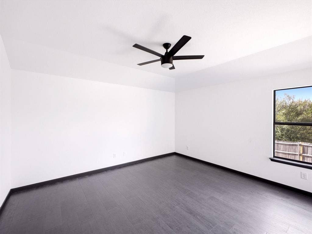 Neutral-toned interior featuring dark wood-finish flooring, white walls, and a matte black ceiling fan with integrated lighting