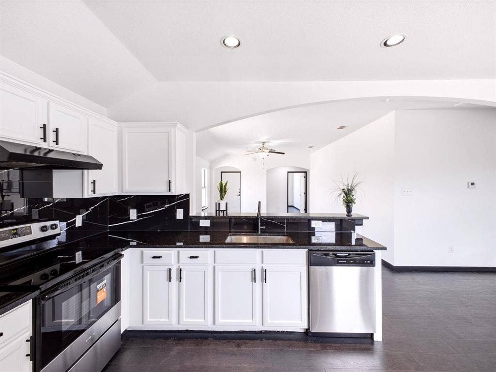 Kitchen featuring white cabinetry with matte black hardware, high-contrast stone-finish backsplash, dark countertops, integrated stainless steel dishwasher, and recessed ceiling lighting