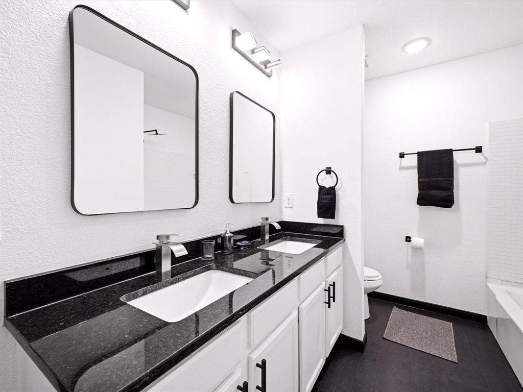 Dual-sink vanity with dark stone countertops, undermount rectangular basins, matte black hardware, and matching wall-mounted mirrors