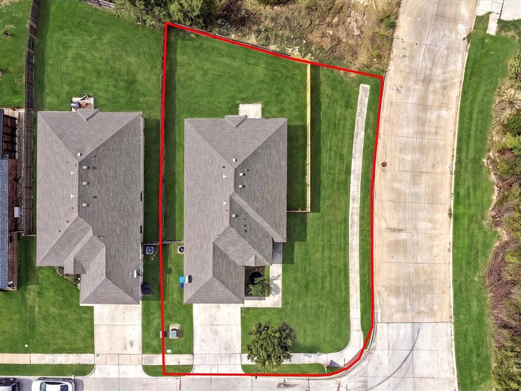 Aerial perspective of a corner lot featuring a shingled roof, concrete driveway, and established grass lawn