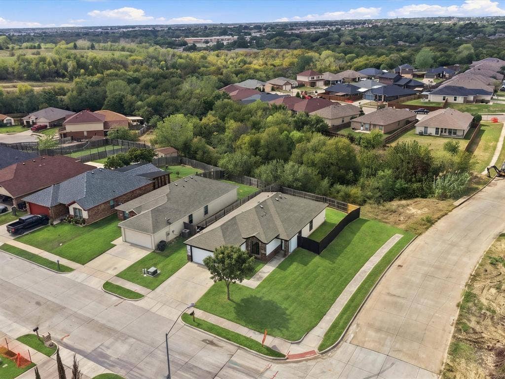 Corner lot featuring a multi-car attached garage, concrete driveway, and expansive lawn, bordered by dense mature trees