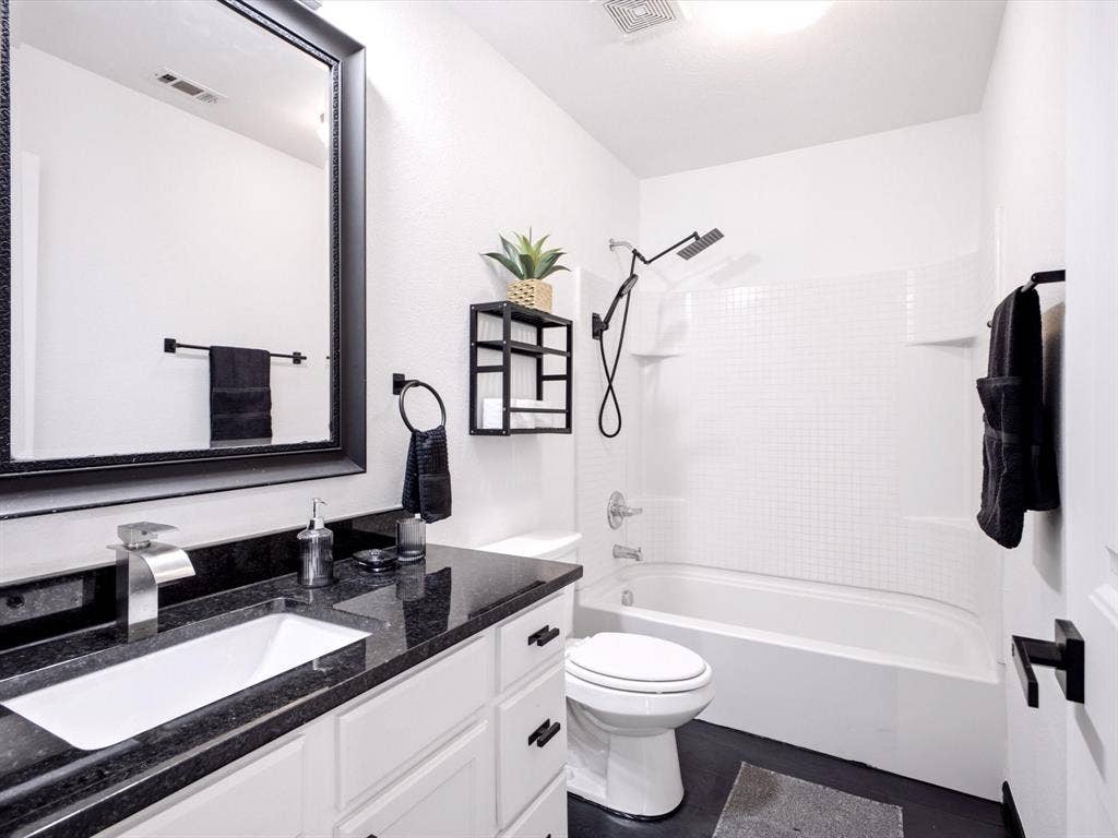 White cabinetry, dark stone vanity countertop, rectangular under-mount sink, matte black faucet and hardware, and shower-tub combination with tile surround