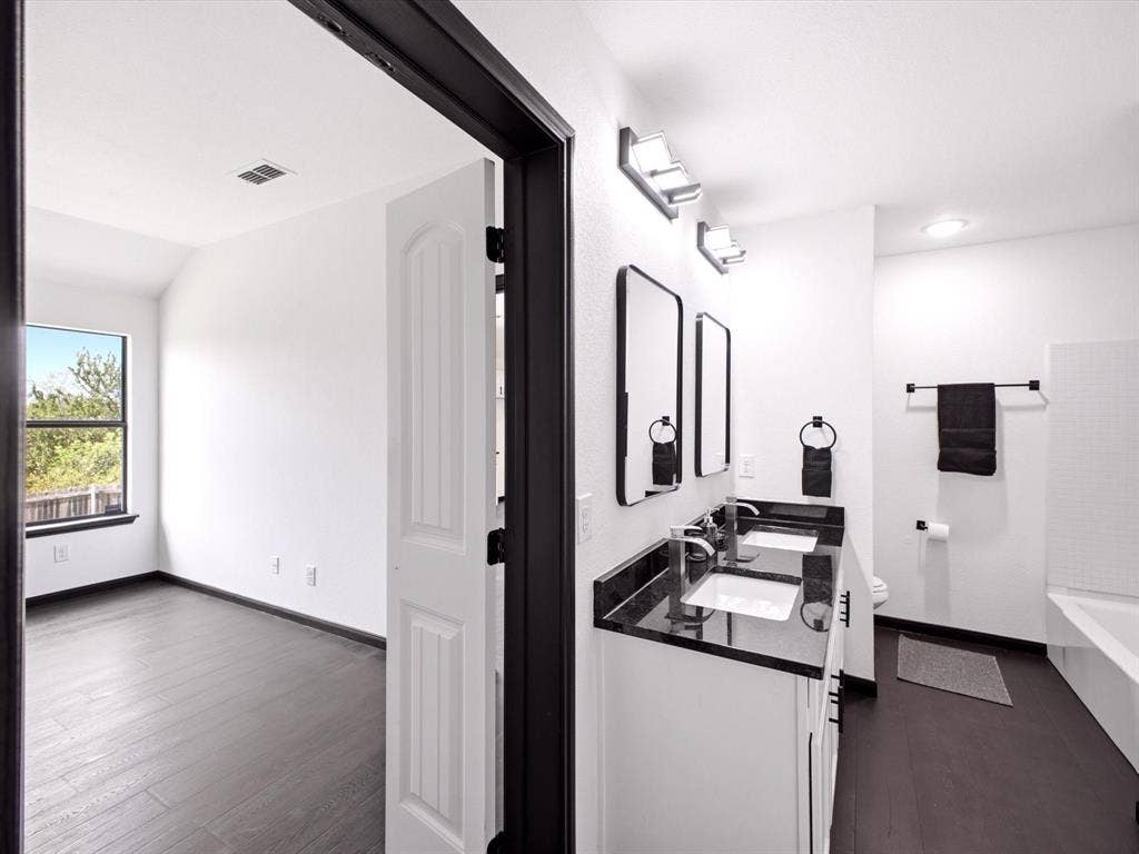 Dual-sink vanity with a dark stone countertop, undermount sinks, sleek rectangular mirrors, and dark-finished hardware
