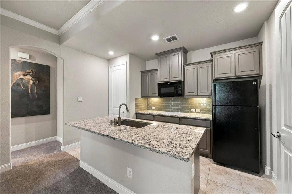 1455 Corrara Drive, Rockwall, TX 75032 Suite Kitchenette features recessed lighting, gray cabinetry, a subway tile backsplash with under-cabinet lighting, a built-in microwave, and a center island with countertops. Ceramic tile flooring extends throughout, transitioning to carpet in the sitting room and hall.
