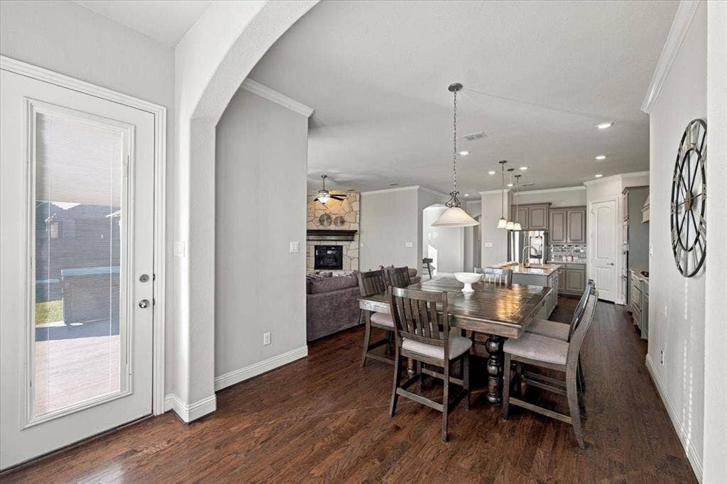 1455 Corrara Drive, Rockwall, TX 75032 Dining Area features a full-lite door to the covered patio and an archway opening to the living room, with an open layout connecting to the kitchen. Wood flooring extends throughout.