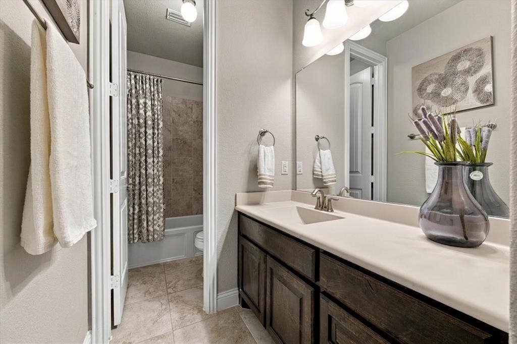 1455 Corrara Drive, Rockwall, TX 75032 Secondary Bathroom features a vanity light fixture, a vanity with countertop and cabinet storage, and a separate compartment with a door, toilet, and tub/shower combination. Ceramic tile flooring extends throughout.