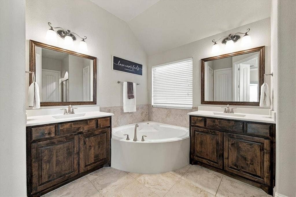 1455 Corrara Drive, Rockwall, TX 75032 Primary Bathroom features dual sinks with countertops and cabinet storage at each vanity, positioned on either side of the garden tub. Ceramic tile flooring extends throughout.