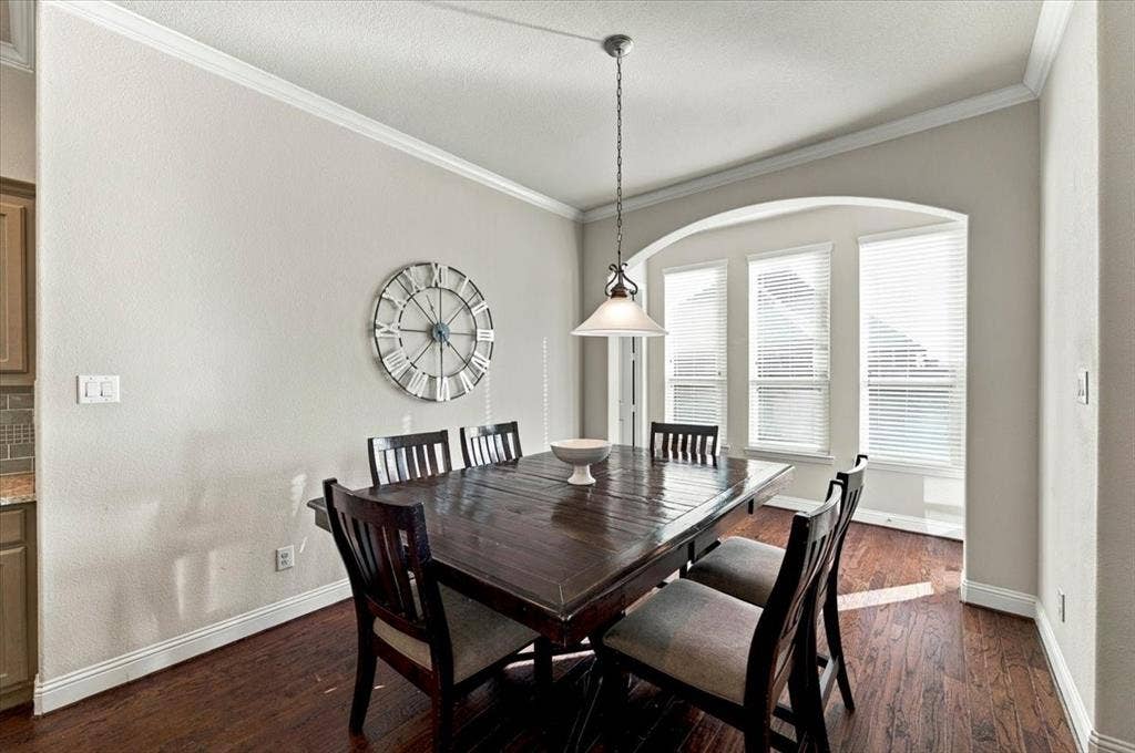 1455 Corrara Drive, Rockwall, TX 75032 Dining Area features crown molding, a pendant light fixture, and an arched alcove with three windows. Wood flooring extends throughout.