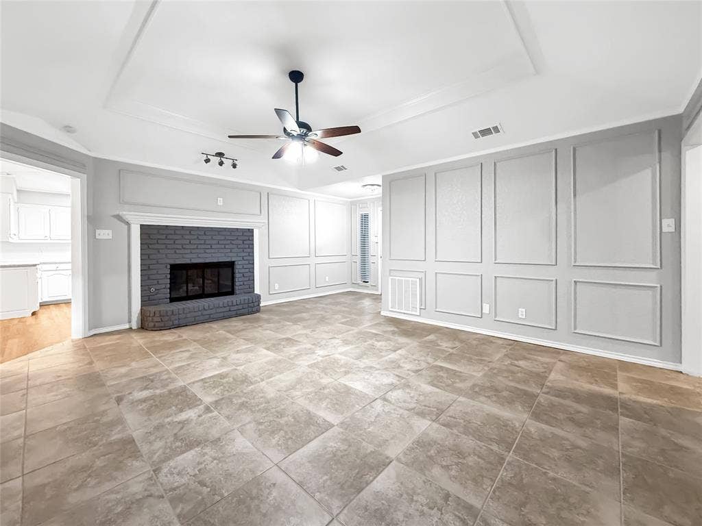 305 N Cottonbelt Avenue, Wylie, TX 75098 Tray ceiling featuring a central ceiling fan, brick fireplace with a decorative mantel, and wall wainscoting complemented by large-format tile flooring