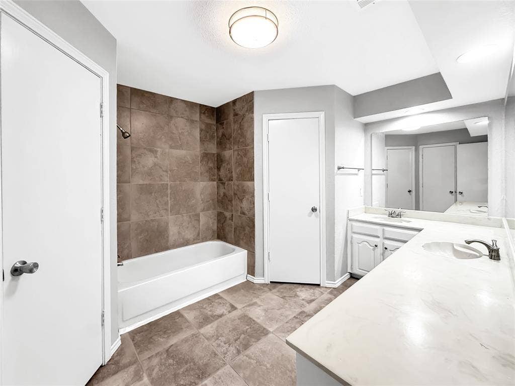 305 N Cottonbelt Avenue, Wylie, TX 75098 Bathroom featuring dual-sink vanity with light-toned solid surface countertop, tub with full-height tile surround, and tile flooring
