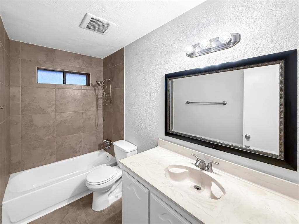 305 N Cottonbelt Avenue, Wylie, TX 75098 Bathroom featuring a vanity with a molded countertop, wall-mounted light fixture, framed mirror, and a tiled shower surround with a handheld shower head