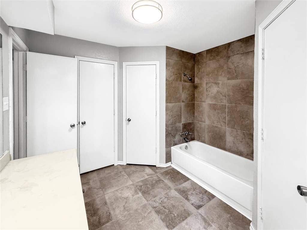 305 N Cottonbelt Avenue, Wylie, TX 75098 Bathroom featuring large-format ceramic floor tile, a deep-set bathtub, full-height wall tiling, a neutral vanity countertop, and a recessed ceiling light fixture