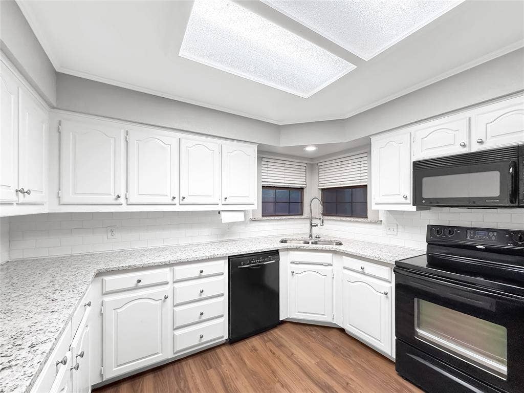 305 N Cottonbelt Avenue, Wylie, TX 75098 Kitchen featuring white cabinetry, light-toned stone-finish countertops, subway tile backsplash, wood-finish flooring, and black appliances