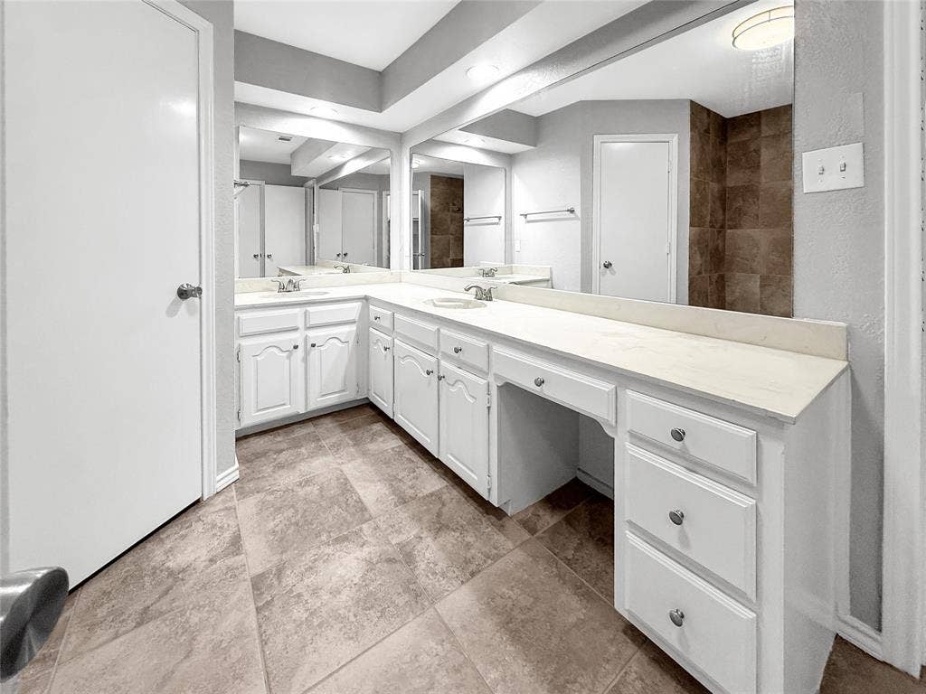 305 N Cottonbelt Avenue, Wylie, TX 75098 L-shaped vanity featuring white cabinetry, a solid surface countertop, dual integrated sinks with chrome fixtures, and a full-width vanity mirror set against tile flooring