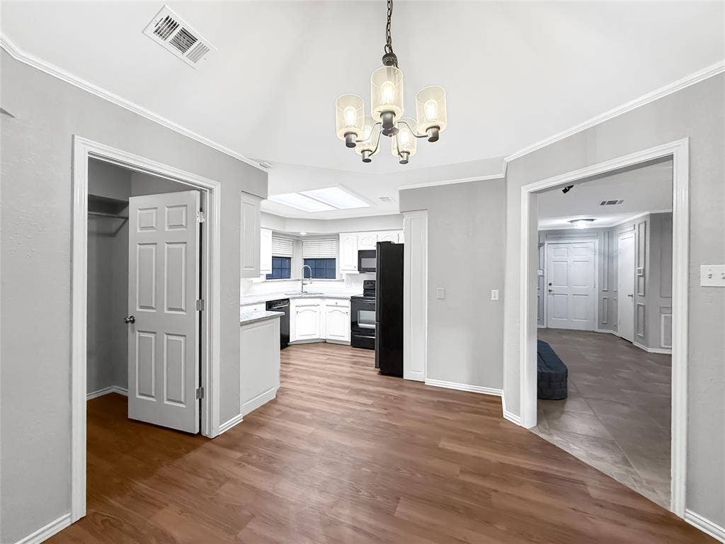 305 N Cottonbelt Avenue, Wylie, TX 75098 Vaulted ceiling with a multi-light chandelier, wood-finish flooring, kitchen featuring built-in cabinetry and a skylight, and multi-panel interior doors