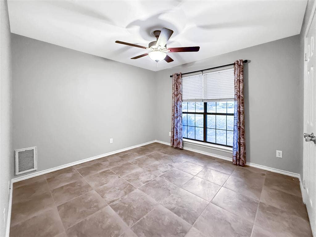 305 N Cottonbelt Avenue, Wylie, TX 75098 Room featuring large-format ceramic floor tile, neutral wall paint, a multi-blade ceiling fan with integrated lighting, and a single-pane window with a grid pattern