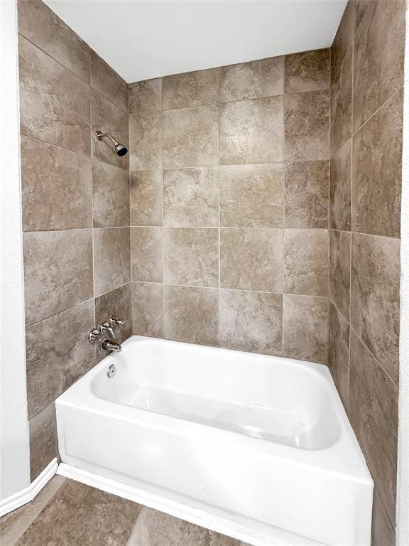 305 N Cottonbelt Avenue, Wylie, TX 75098 Bathtub surround featuring floor-to-ceiling square earth-tone wall tiles, a built-in white acrylic tub, and polished chrome plumbing fixtures