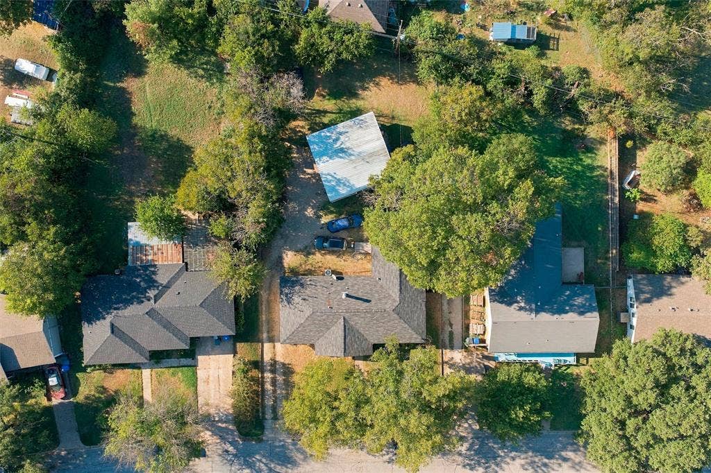 Aerial perspective of a residential lot featuring a multi-gabled roofline, a detached metal-sided structure, concrete driveways, and mature tree canopy coverage
