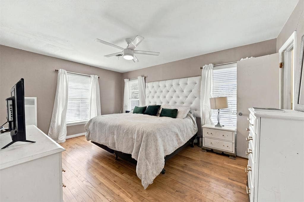 Room featuring wood-finish flooring, three windows with horizontal blinds, and a white ceiling fan with integrated lighting
