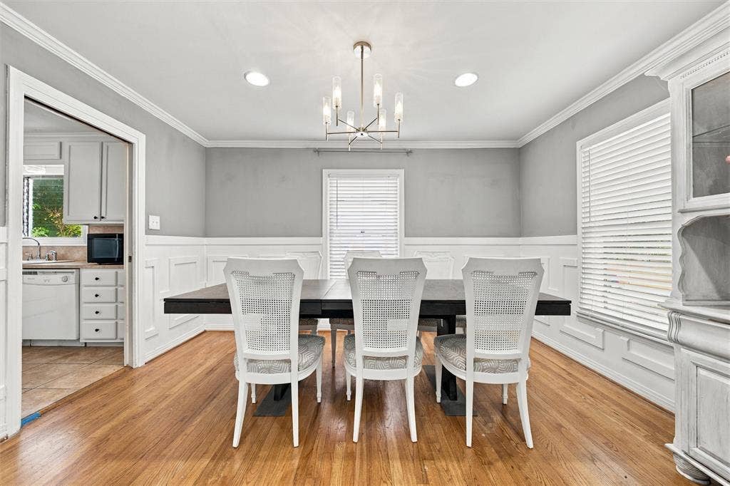 Dining room featuring wood-finish flooring, white wainscoting, crown molding, and a central multi-arm light fixture
