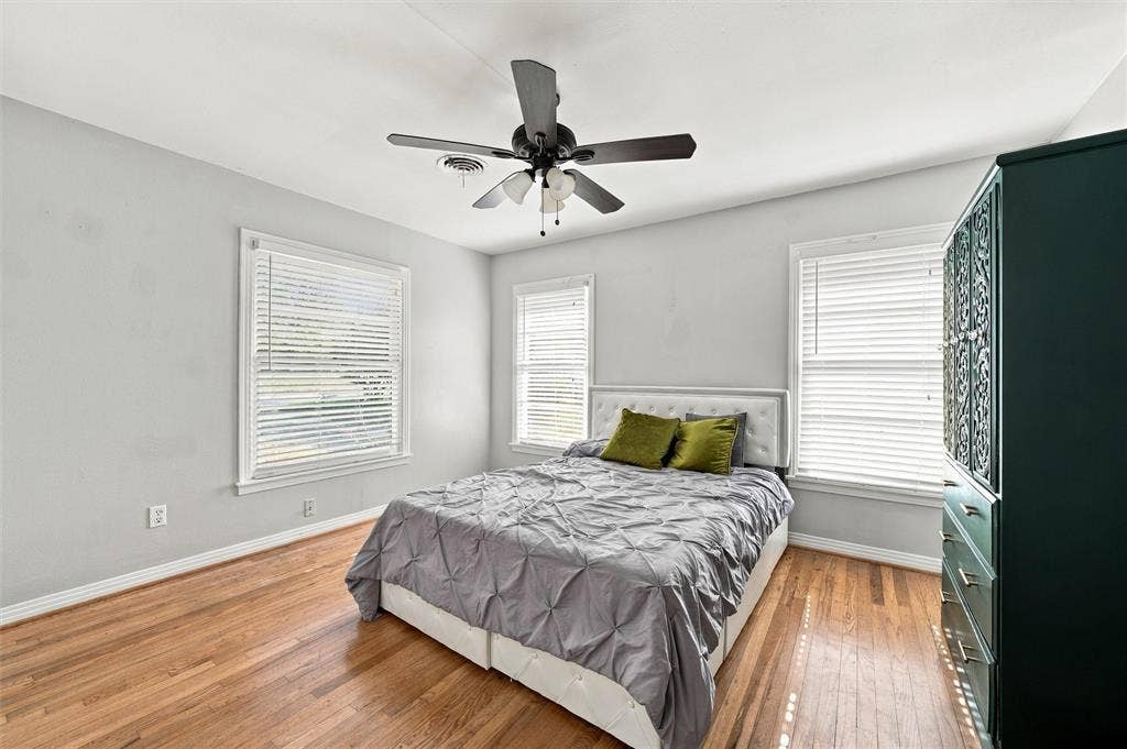 Wood-finish flooring, neutral wall tones, multi-window configuration with horizontal blinds, and a central ceiling fan with integrated lighting