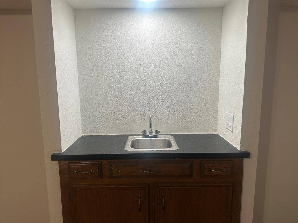 Built-in wet bar featuring a recessed alcove, dark countertop, stainless steel drop-in sink, and wood-finish cabinetry
