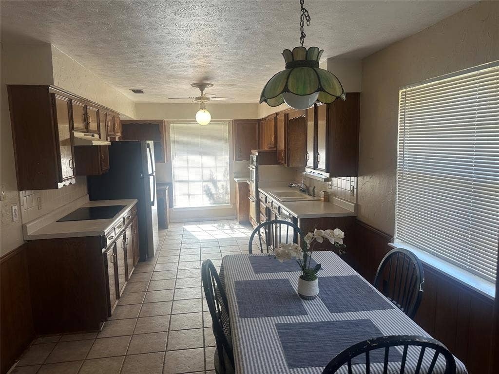 Kitchen featuring wood cabinetry, tile flooring, built-in cooktop, wall-mounted oven, and decorative pendant lighting
