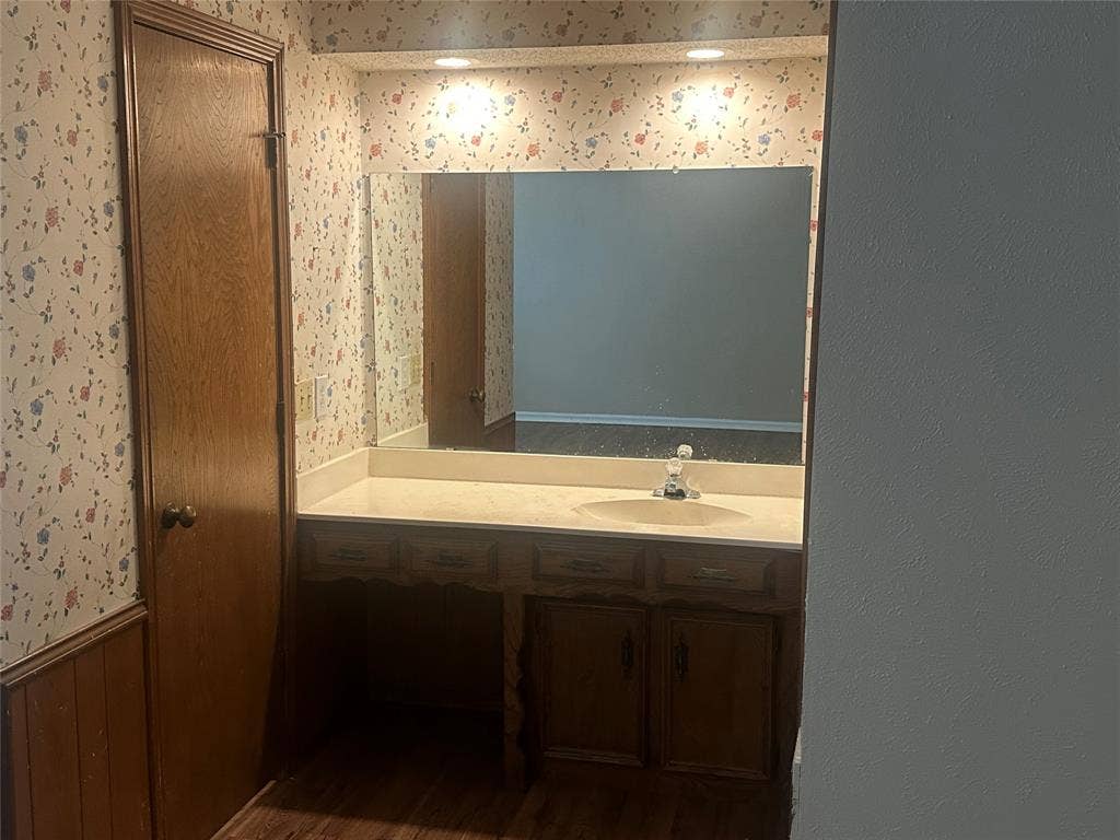 Vanity featuring wood cabinetry, integrated basin, countertop, and a large-format mirror with recessed lighting