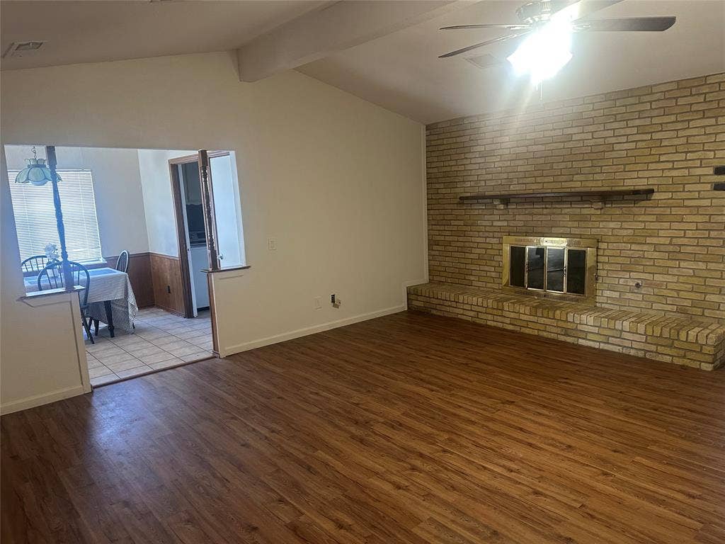 Vaulted ceilings, wood-finish flooring, floor-to-ceiling brick fireplace with a hearth, and a ceiling fan