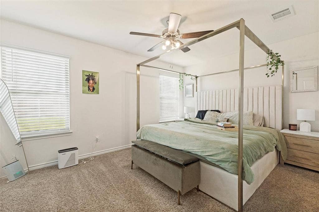 Neutral-toned wall-to-wall carpeting, dual windows with horizontal blinds, and a ceiling-mounted light fixture with a fan
