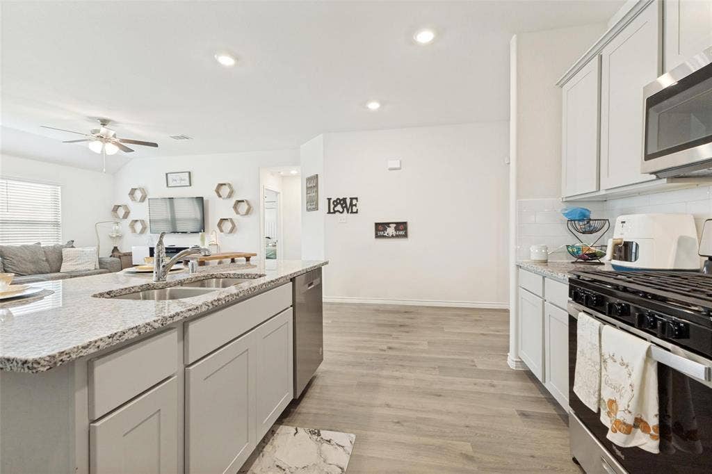 Kitchen featuring a large central island with a double-basin sink, light-toned cabinetry, stone-finish countertops, stainless steel appliances, and wood-finish flooring