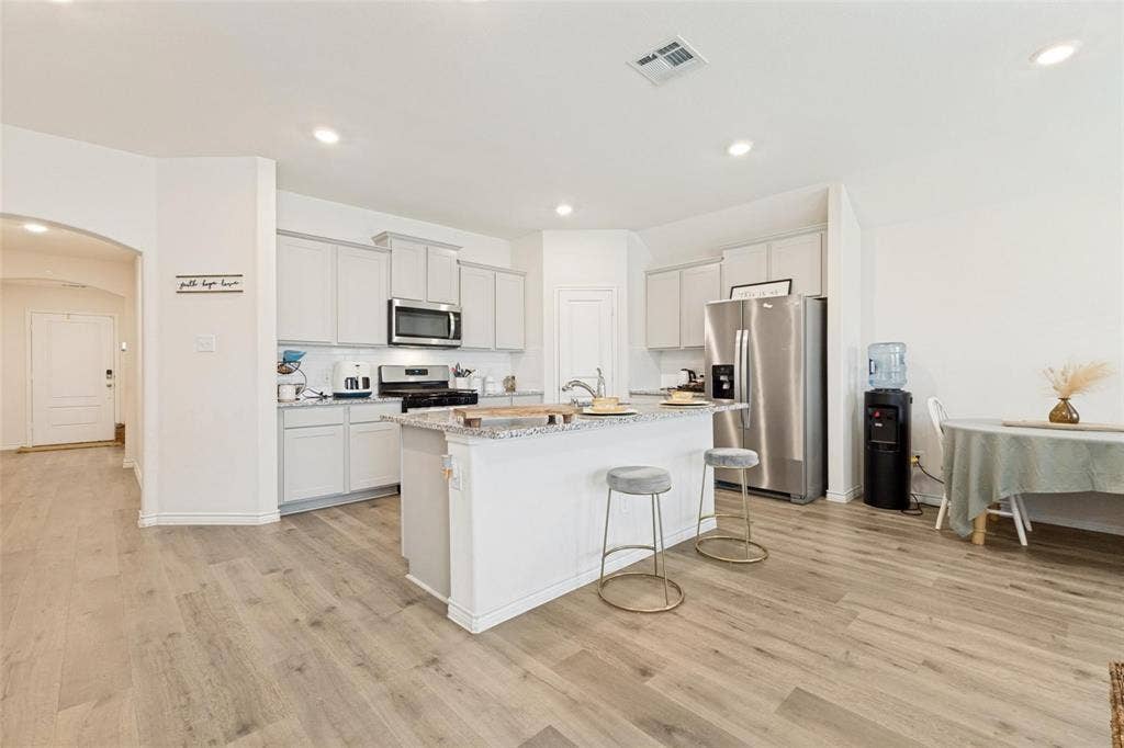 Kitchen featuring a central island with a stone-finish countertop, light-toned cabinetry, recessed lighting, and wood-finish flooring