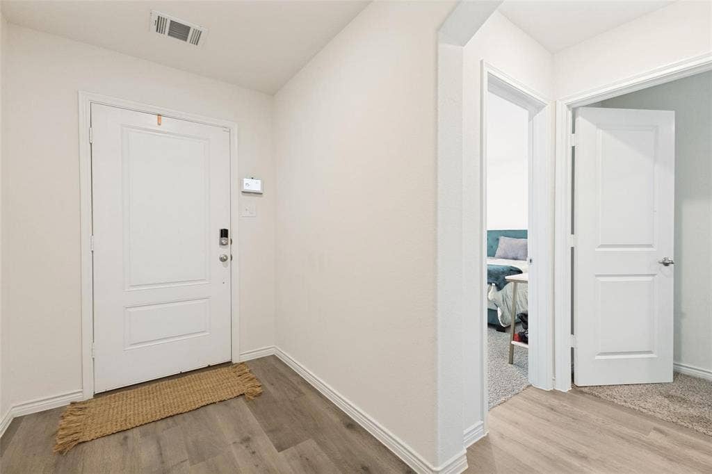 Entryway featuring wood-finish flooring, a paneled door with integrated electronic lock, and crisp white interior trim