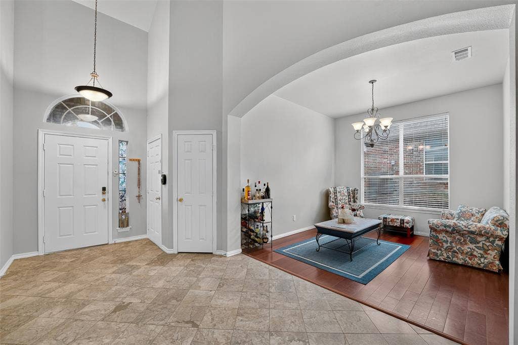 Foyer featuring soaring ceilings, a decorative transom window, natural stone-style tile flooring, wood-finish flooring, and an arched architectural opening