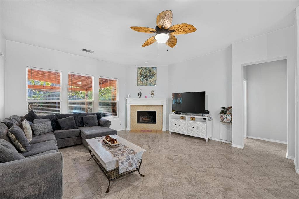 Living area featuring tile flooring, a central fireplace with a decorative surround, and a ceiling fan with leaf-patterned blades