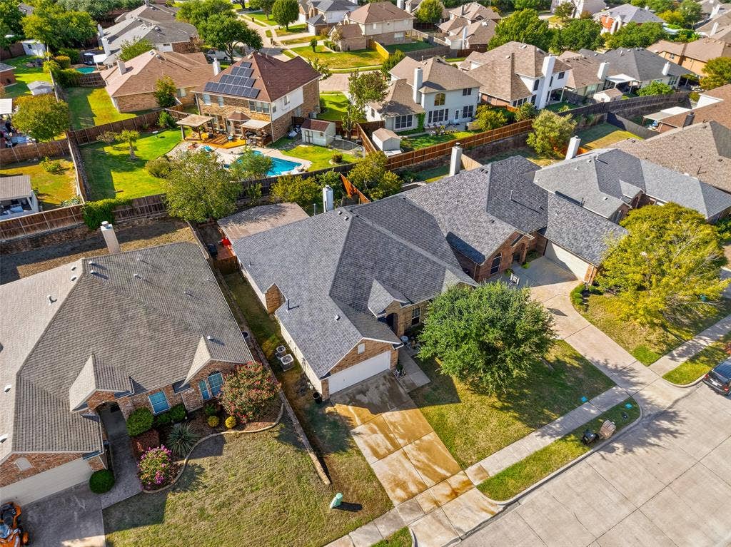 Aerial perspective featuring a multi-hipped asphalt shingle roof, masonry exterior, multi-car garage, concrete driveway, and established landscape