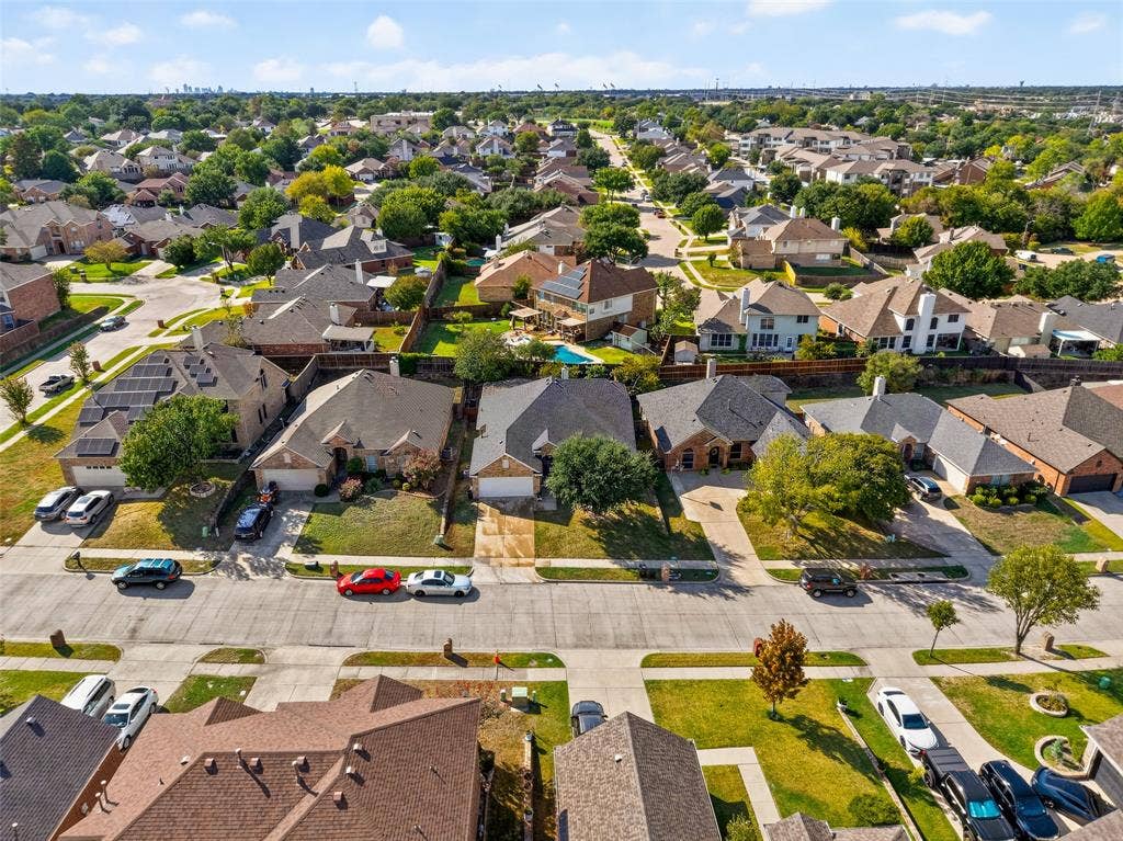 Aerial perspective of a suburban neighborhood featuring brick and masonry residential exteriors, pitched shingle roofing, integrated garage structures, and mature tree-lined streets