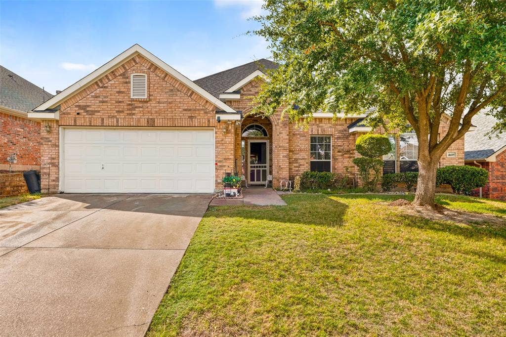 Brick exterior featuring a gabled roofline, a multi-pane arched entryway, a double-car garage, and established landscaping