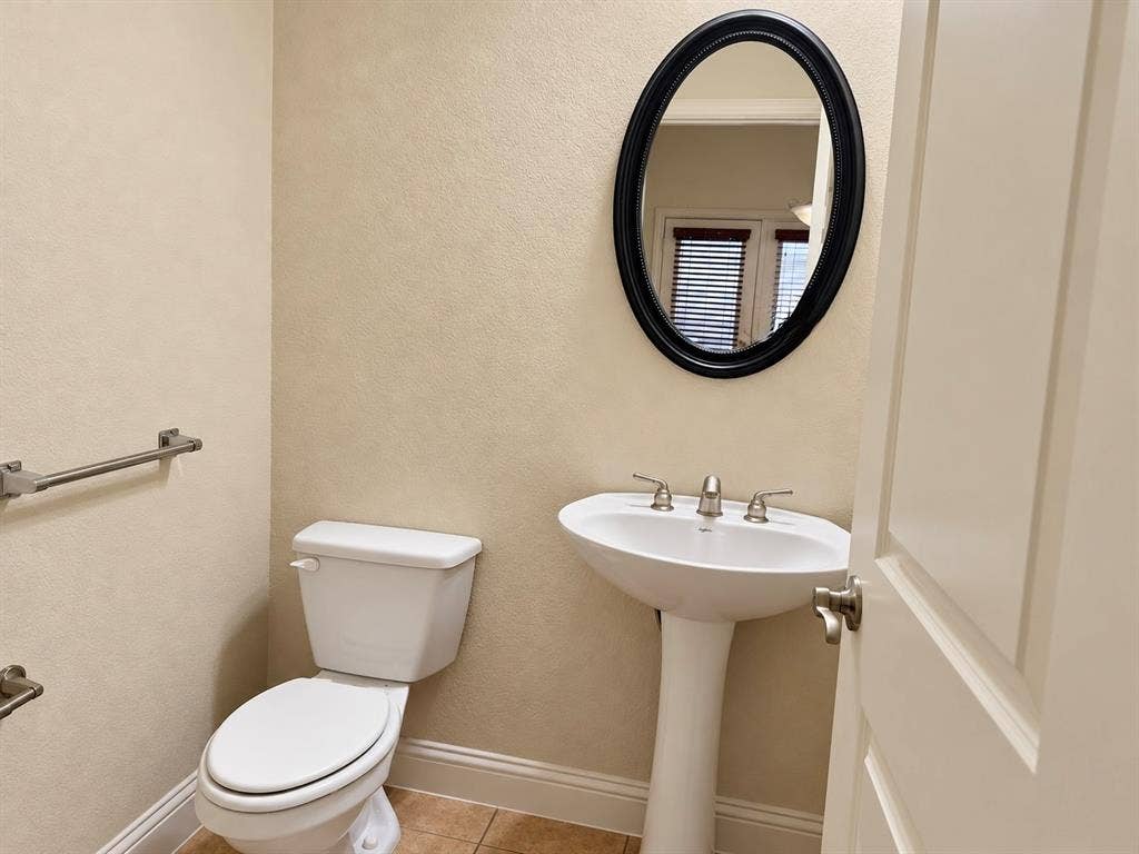 8616 Naomi Street, Plano, TX 75024 Pedestal sink with a widespread faucet, oval wall mirror with a black frame, ceramic tile flooring, and brushed nickel hardware