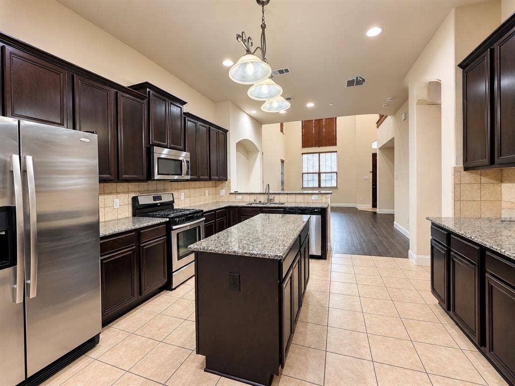 8616 Naomi Street, Plano, TX 75024 Kitchen featuring dark wood cabinetry, stone countertops, central island, stainless steel appliances, and tile flooring