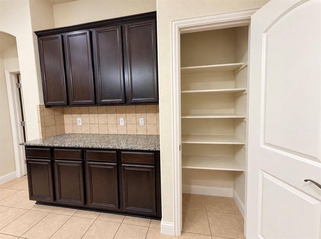 8616 Naomi Street, Plano, TX 75024 Dark wood cabinetry with stone-finish countertops, square-tile backsplash, and walk-in pantry with multi-level shelving
