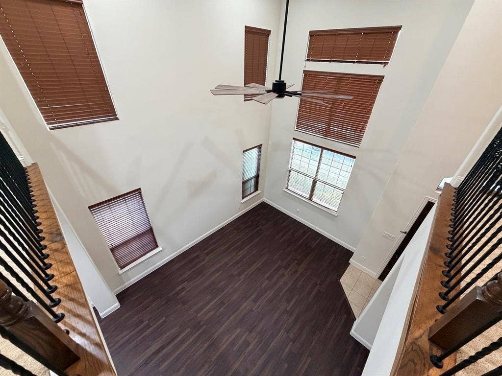 8616 Naomi Street, Plano, TX 75024 Double-height ceiling featuring wood-finish flooring, multiple oversized windows, wooden slat blinds, and a suspended ceiling fan