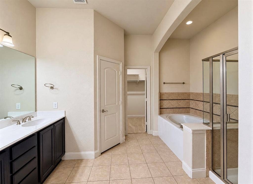 8616 Naomi Street, Plano, TX 75024 Bathroom featuring dark-finish cabinetry with a white countertop, undermount dual sinks, a jetted soaking tub with tile surround, and a glass-enclosed shower