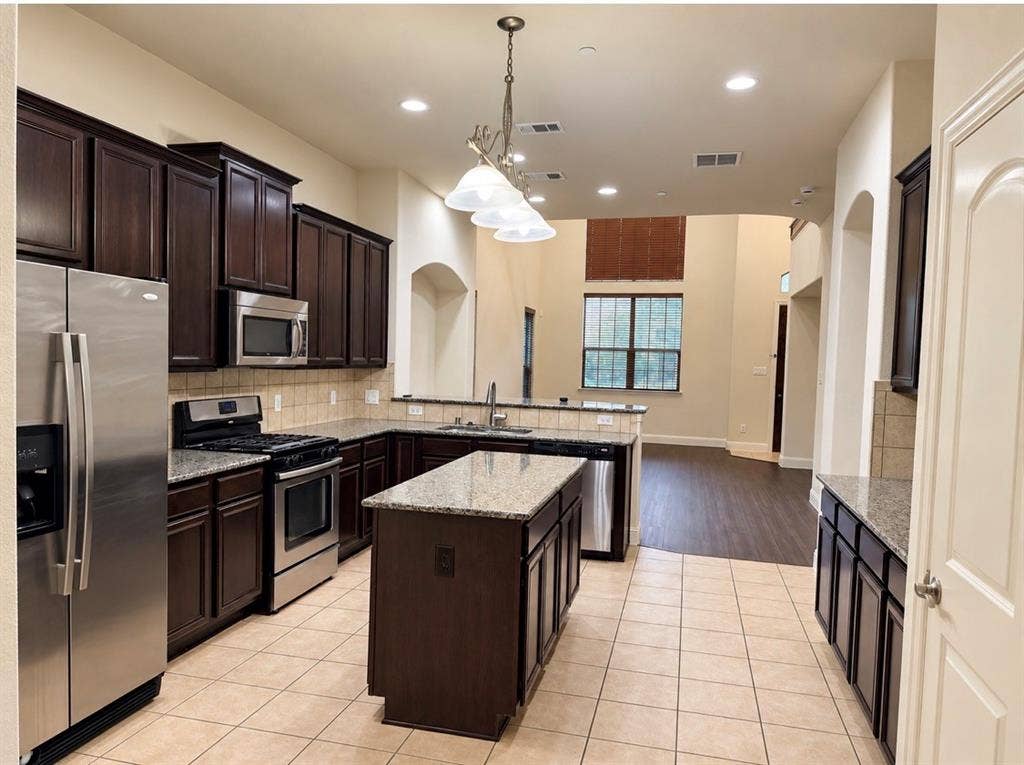 8616 Naomi Street, Plano, TX 75024 Kitchen featuring dark wood cabinetry, an expansive center island, stone-finish countertops, stainless steel appliances, and tile flooring