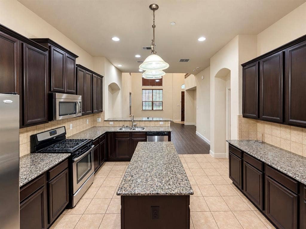 8616 Naomi Street, Plano, TX 75024 Kitchen featuring dark-finish cabinetry, stone countertops, a central island, stainless steel appliances, and tile flooring