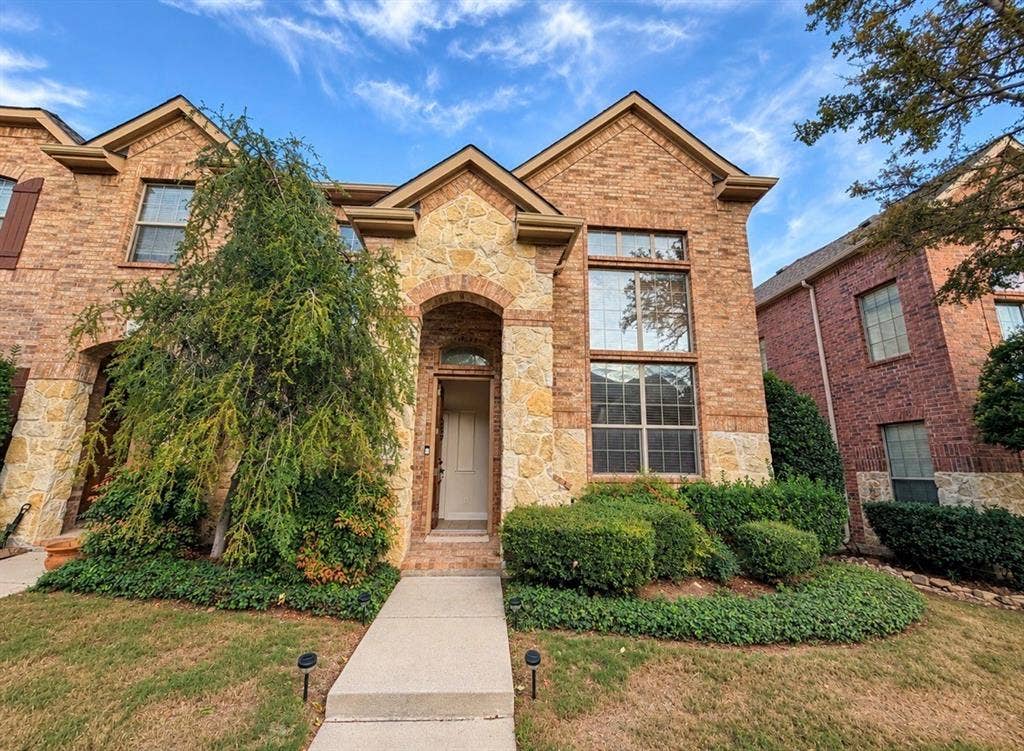 8616 Naomi Street, Plano, TX 75024 Two-story brick and stone facade featuring an arched entryway, multi-pane windows, and a concrete front walkway