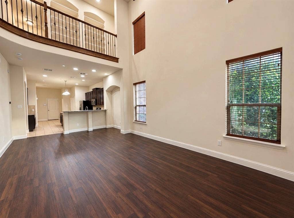 8616 Naomi Street, Plano, TX 75024 Double-height ceiling, wood-finish flooring, wrought iron staircase railing, recessed lighting, and built-in kitchen cabinetry with a breakfast bar