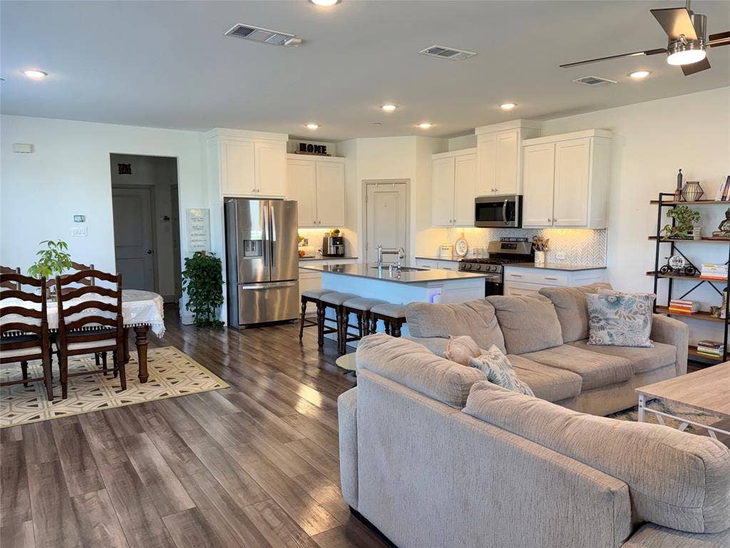 9096 Phoebe Road, Frisco, TX 75035 Open-concept interior featuring wood-finish flooring, white cabinetry, stainless steel appliances, a central kitchen island with countertop seating, and recessed lighting